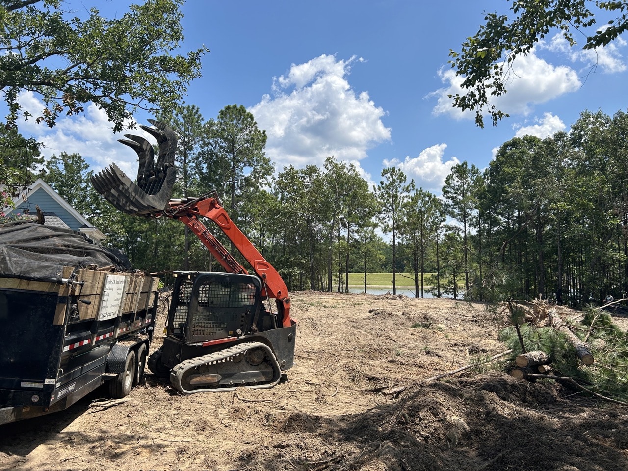 Excavator with claw attachment parked next to a truck on a cleared construction site.