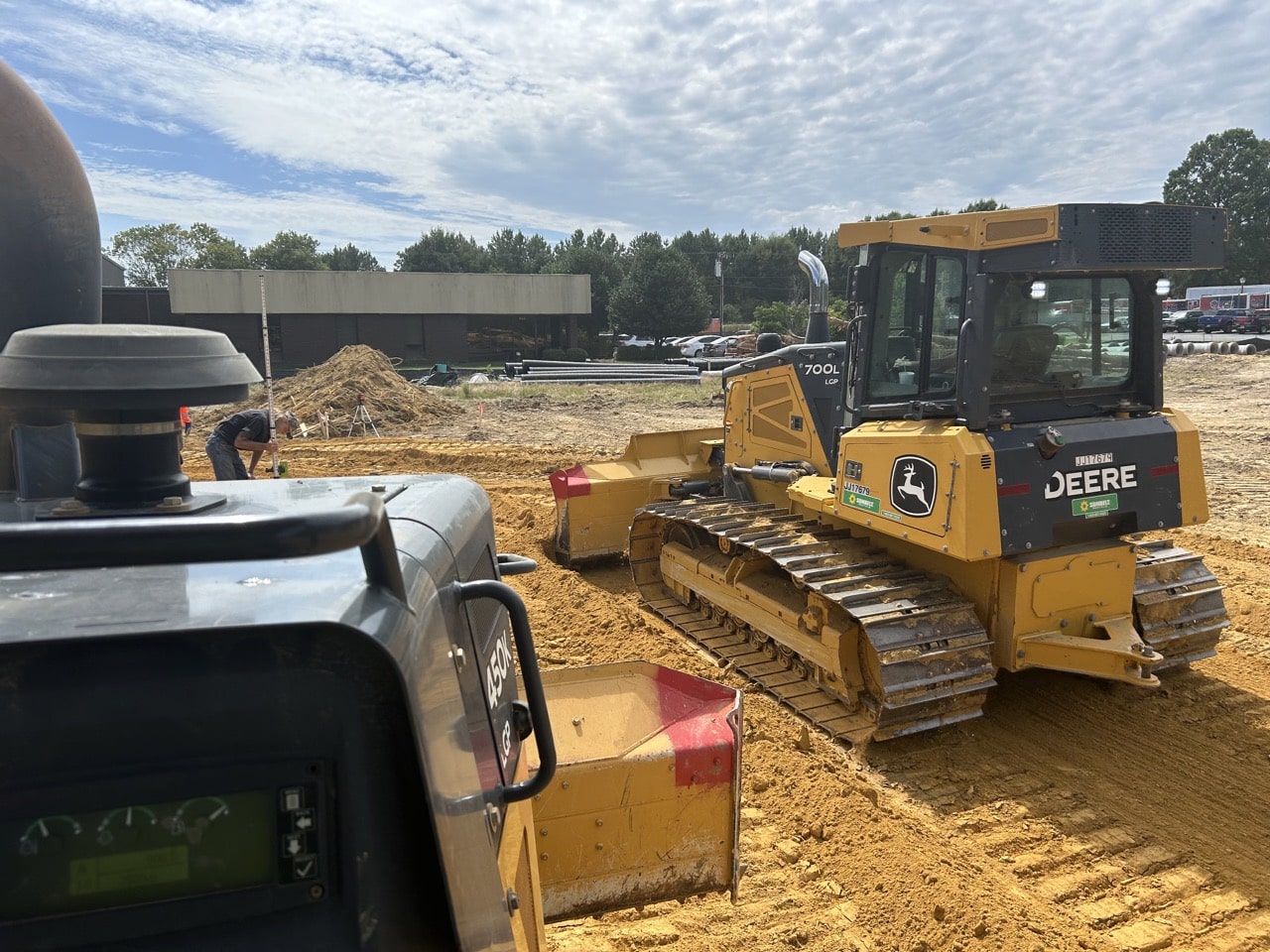 John Deere 700L crawler dozer moving earth on a construction site with another machine in view.