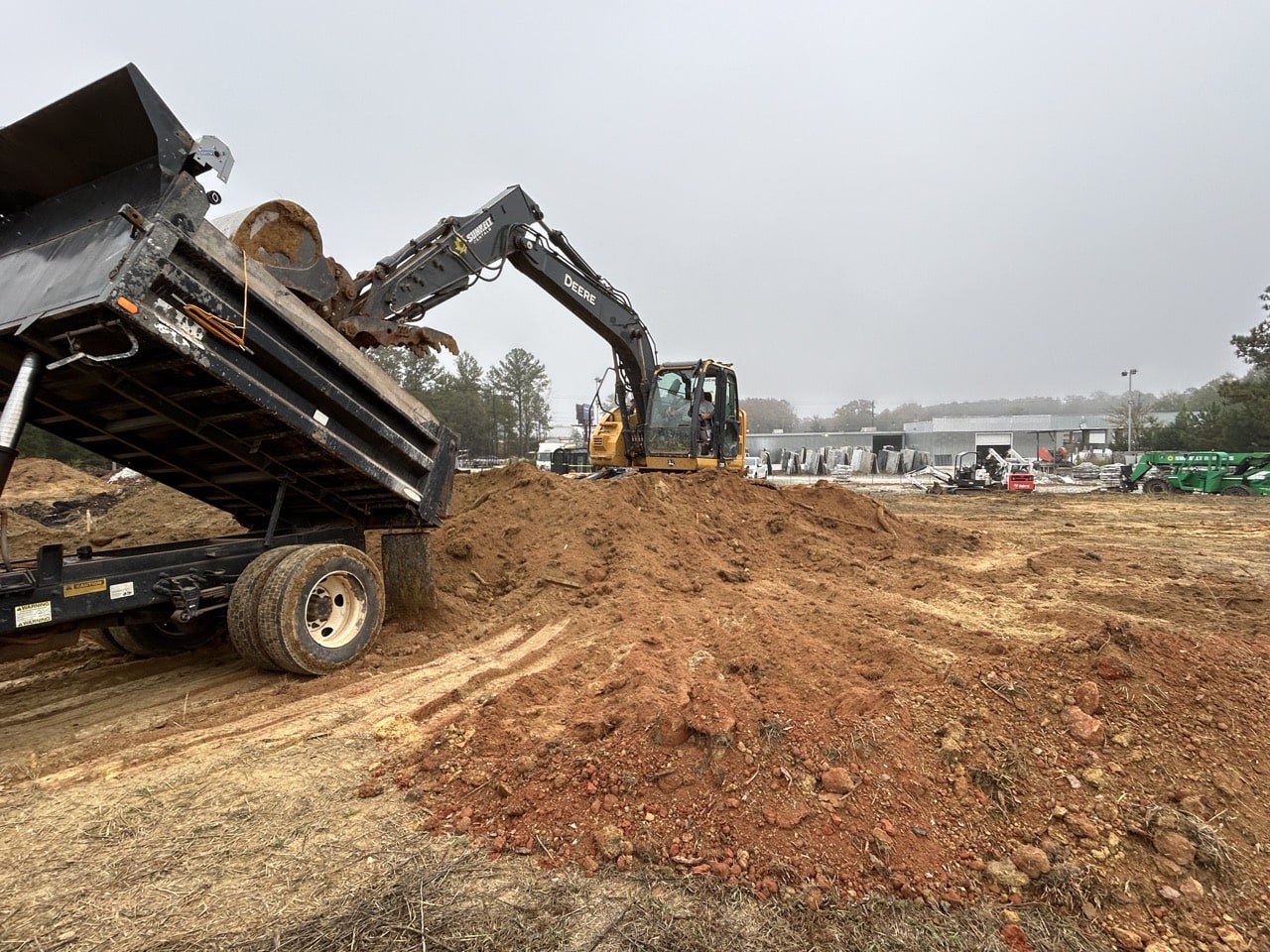 Excavator loading dirt from a dump truck on a construction site with machinery in the background.